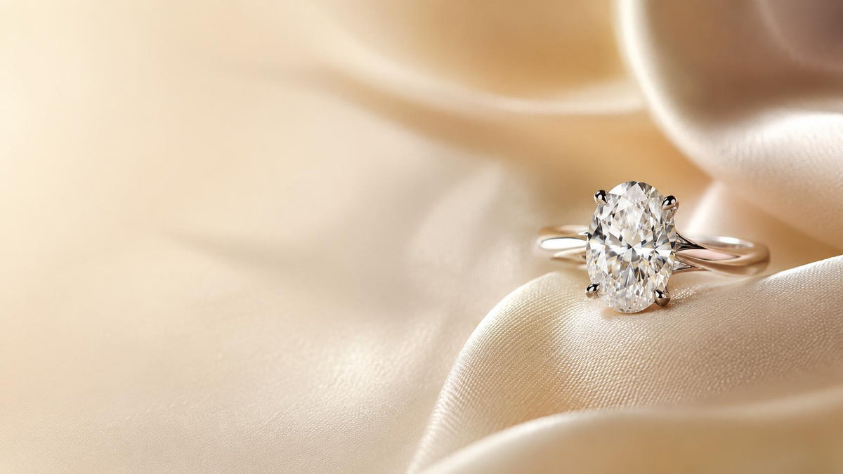 An oval diamond ring rests on ivory fabric.